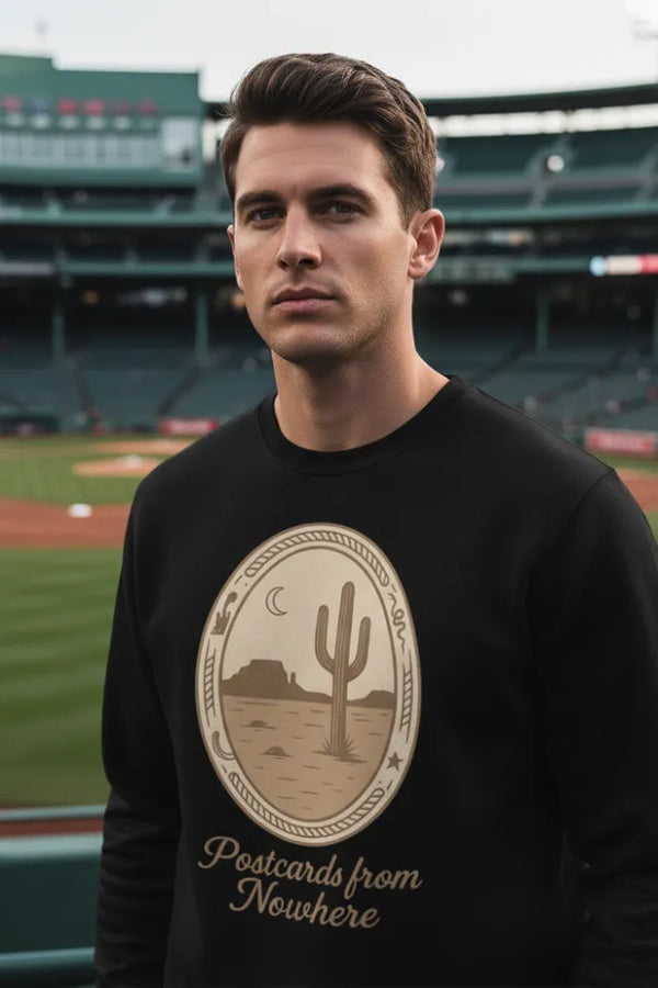 Man wearing a black sweatshirt with a cactus design and text at a baseball stadium.