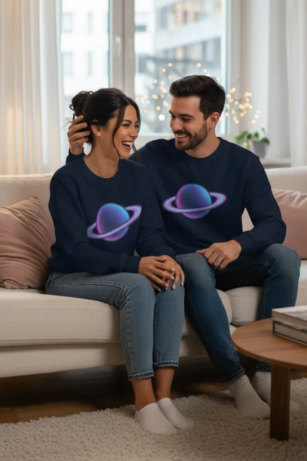 Two people sitting on a couch wearing matching navy blue sweatshirts with planet designs.