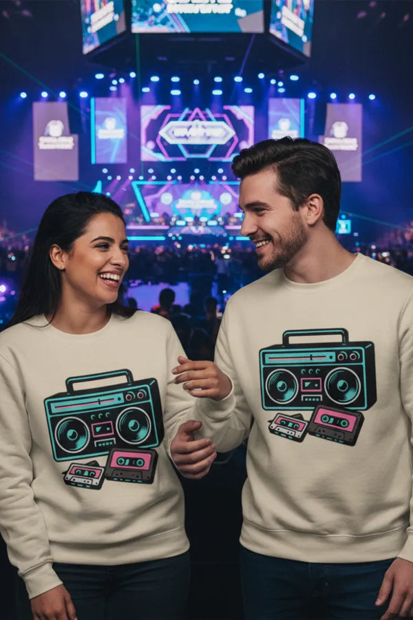 Two people wearing matching sweatshirts with boombox designs in a concert setting.