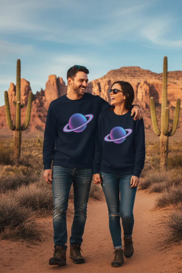 Two people wearing matching dark blue sweatshirts with a colorful planet design, standing in a desert landscape with cacti and mountains.