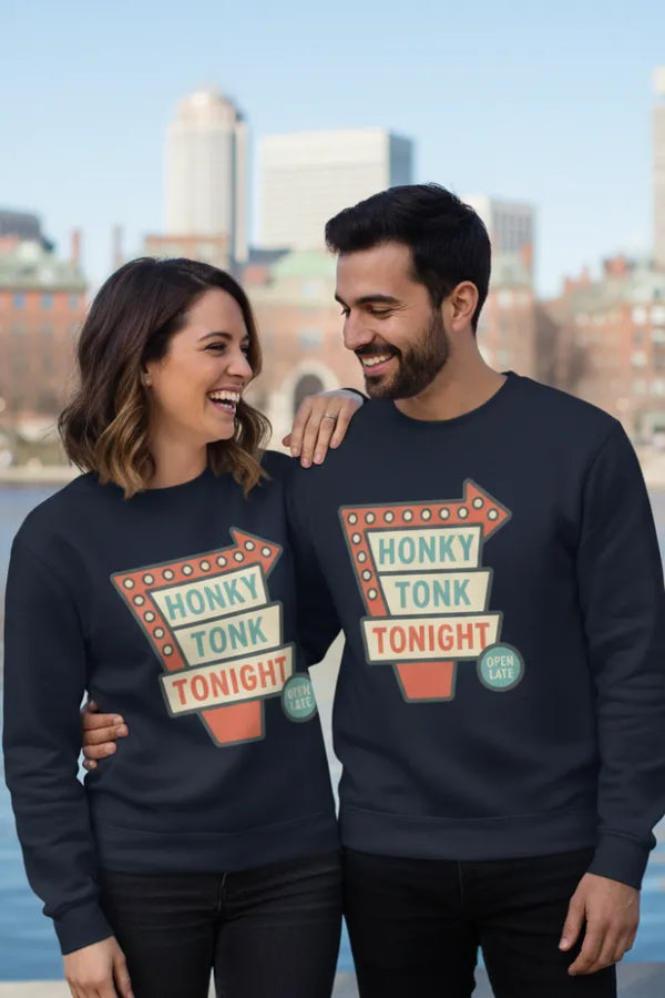 Two people wearing navy blue sweatshirts with 'Honky Tonk Tonight' design, standing by a waterfront with a city skyline in the background.