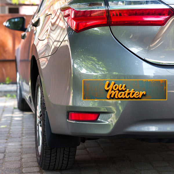 Close-up of a car featuring the "You Matter" inspirational bumper sticker with vibrant orange text on a rustic blue background. A motivational message perfect for spreading positivity on the go.