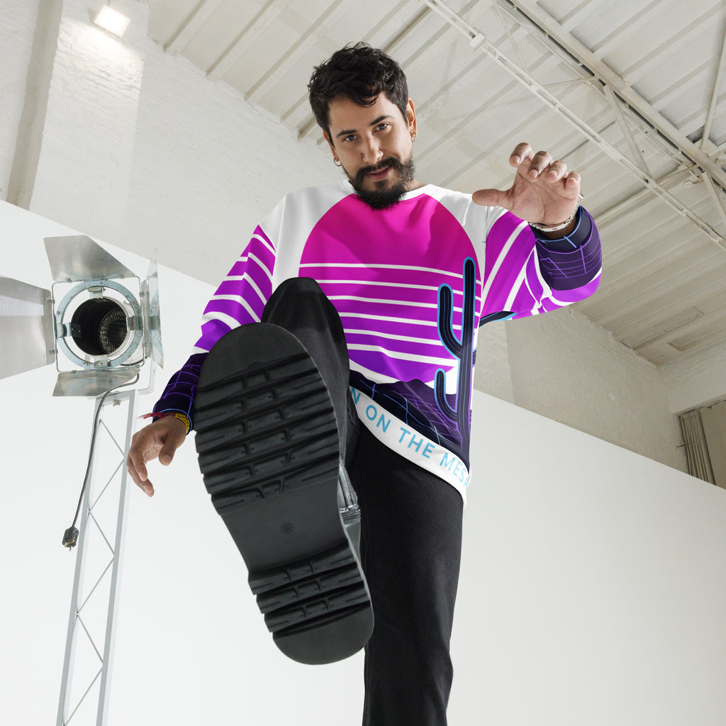 Man wearing a colorful shirt with a cactus design, holding up a black shoe in a studio setting.