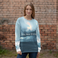 Woman wearing a sweater with 'You Are Enough' text against a brick wall.