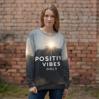 Person wearing a sweater with 'Positive Vibes Only' text against a brick wall.