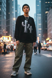 Person wearing a black sweatshirt with a cactus graphic on a city street at night.