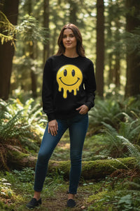 Woman wearing a black sweatshirt with a yellow smiley face design in a forest setting