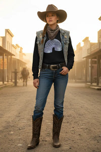 Woman in cowboy hat and boots standing on a dusty street with western-style buildings.