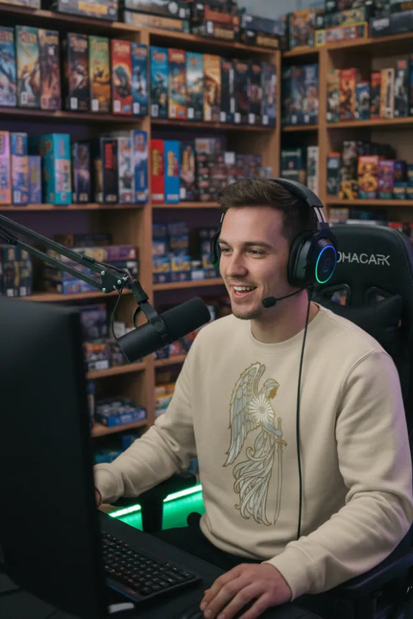 Person sitting in front of a computer with gaming equipment, surrounded by shelves filled with video games.