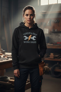 Person wearing a hoodie with 'Torque & Grit Work Hard' text in a workshop setting