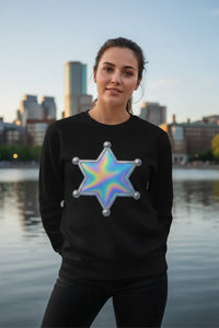 Person wearing a black sweatshirt with a colorful star design, standing by a waterfront with city skyline in the background.