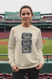 Woman wearing a beige sweatshirt with a graphic design of eyes on a sports field background