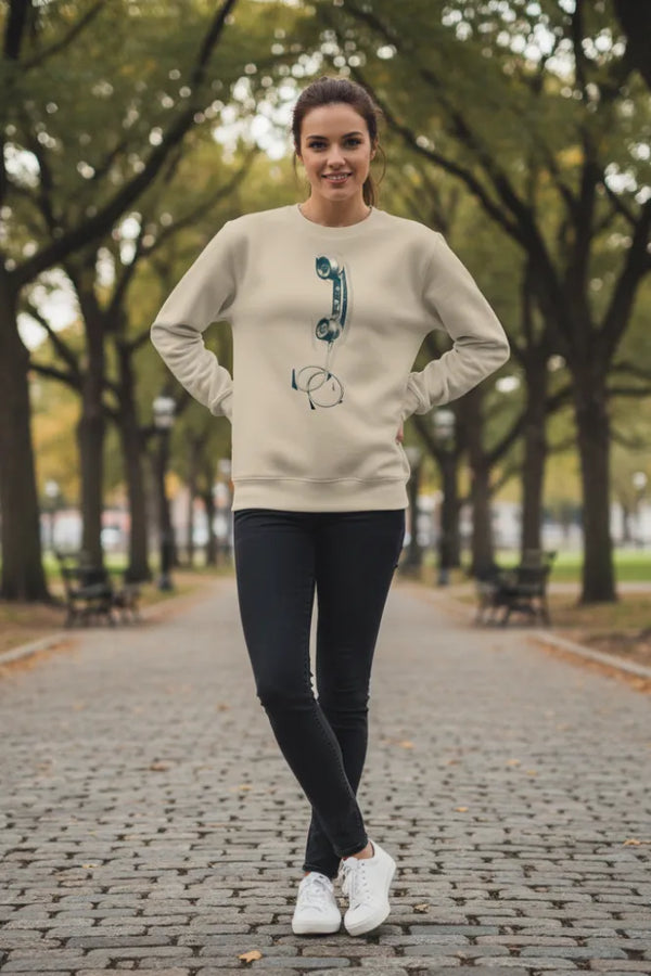 Woman wearing a cream sweater with a graphic design, black pants, and white sneakers standing on a tree-lined path.