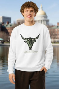 Person wearing a white sweatshirt with a bull graphic and 'Bloom & Range' text, standing by a body of water with a building in the background.
