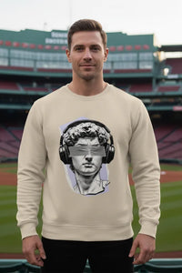 Man wearing a beige sweatshirt with a graphic design of a classical statue wearing headphones in front of a stadium.