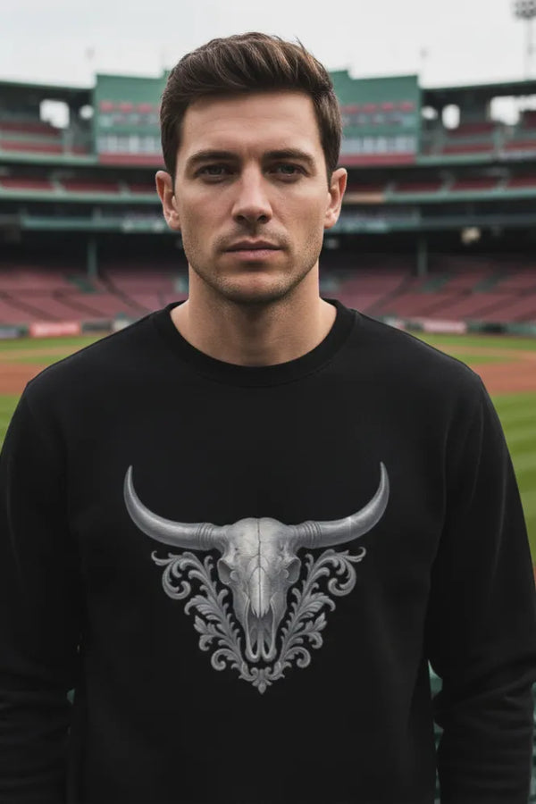 Man wearing a black sweatshirt with a bull skull design in an outdoor stadium setting