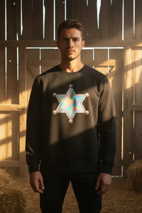 Man wearing a black sweatshirt with a colorful star design in a barn setting