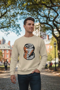 Man wearing a beige sweatshirt with a graphic design of a can, standing in an outdoor setting with trees and buildings.