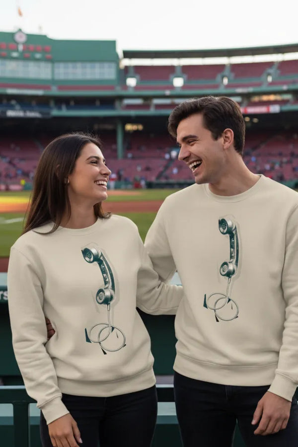 Two people wearing matching sweaters with a design of a phone receiver and headset at a baseball stadium.