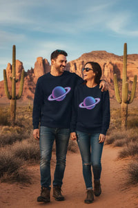 Two people wearing matching dark blue sweatshirts with a colorful planet design, standing in a desert landscape with cacti and mountains.